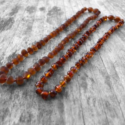 2 coliere unisex pentru adulti din chihlimbar baltic maro coniac, mat si lucios prezentate pe fundal din lemn