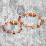 set bratari familie chihlimbar maro cu snur rosu pe fundal lemn