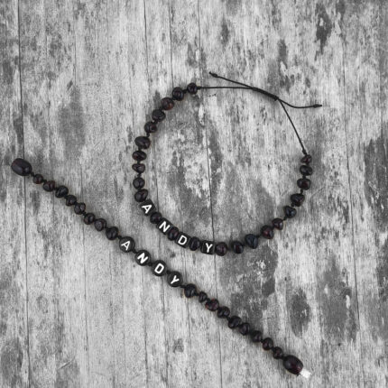 set bratari copil adult din chihlimbar negru personalizate cu nume expuse pe fundal de lemn