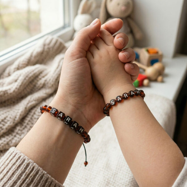 set 2 bratri personalizate cu nume din chihlimbar baltic maro coniac prezentate pe mana unei mame si a bebelusului