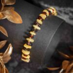 Brățară din chihlimbar cu pepite negre și de culoarea untului, aranjate alternativ pe un snur elastic, prezentată pe fundal negru.