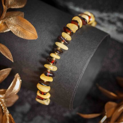 Brățară din chihlimbar cu pepite negre și de culoarea untului, aranjate alternativ pe un snur elastic, prezentată pe fundal negru.