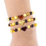 Trei brățări din chihlimbar natural cu pandantive în formă de inimă, purtate la încheietura mâinii – eleganță și energie naturală într-un design rafinat.