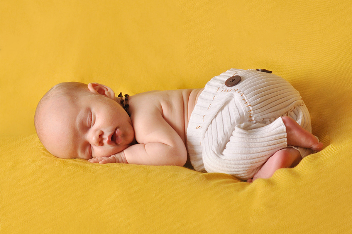 imagine lifestyle pe fundal galben cu bebelus dormind linistit purtand cun colier din chihlimbar la gat